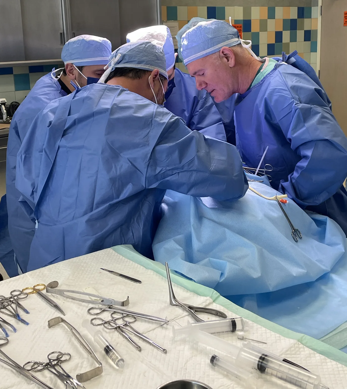 Three surgeons operating together at the table, instrument tray in the foreground